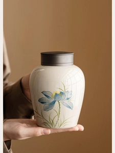 Detail of hand-painted blue lotus on ceramic tea canister held by hands with matte lid