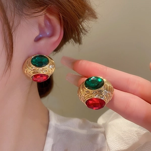 Detail of vintage gold earrings with deep green and red gemstones in a retro style