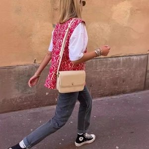 Outdoor street view of a woman wearing a red geometric print vest and casual grey jeans