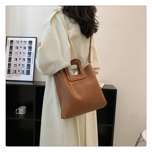 Brown leather bucket bag with square cutout handle shown on shoulder in minimalist setting