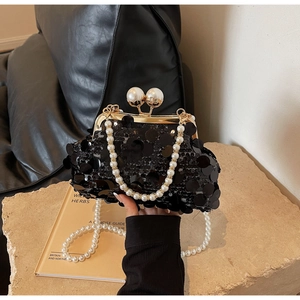 Detail of black sequined clutch bag with gold frame and large pearl clasp closure