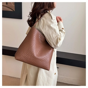 Detail of a brown woven leather tote bag worn with a beige trench coat on a shoulder