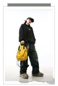 Detail of the yellow nylon backpack featuring multi-pockets and black straps on a model