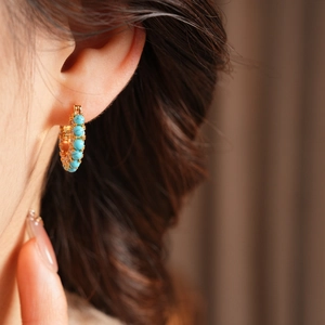 Close-up of 18k gold plated hoop earring with turquoise stone inlay on a model