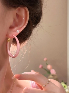 Close-up of pink enamel hoop earrings and gold rings on a model with flowers