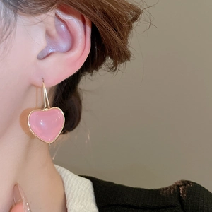 Close-up of pink resin heart earring with gold metal trim worn on a model's ear