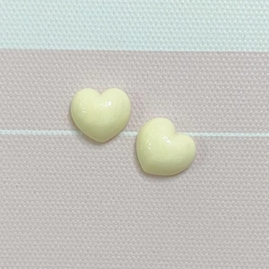 Close-up of two polished heart-shaped resin charms in creamy beige on striped fabric