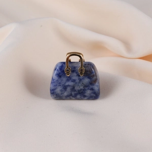 Detailed close-up of blue stone handbag pendant with golden handle on soft fabric