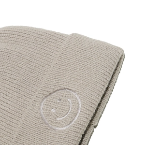 Detailaufnahme der beigen Strickmütze mit weißem Smiley-Stickerei auf dem gerippten Umschlag