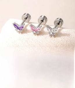 Macro shot of zircon butterfly ear studs in purple, pink, and clear tones with steel stems
