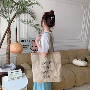 Detail of beige canvas tote bag showing 'draw your every day' print and green embroidery