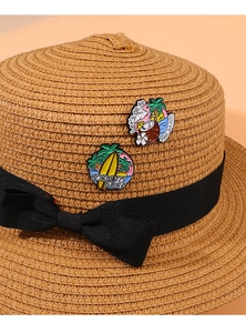Detail of summer palm tree and surf enamel pins pinned on a woven straw beach hat