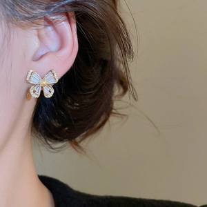 Detailed close-up of a gold-plated butterfly earring with zircon and pearl on a model's ear