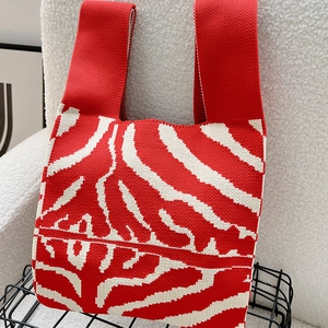 Close-up of red and beige zebra striped knitted tote bag on white fleece surface