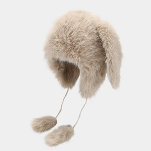 Close-up of beige plush winter hat with fluffy earflaps and soft decorative pom-poms