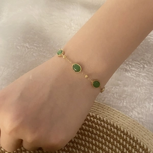 Close-up of a gold-plated bracelet with oval green emerald stones worn on a wrist