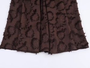 Detail aus dunkelbraunem Jacquard-Stoff mit 3D-Blumenstruktur und Fransen am Saum des Kleides