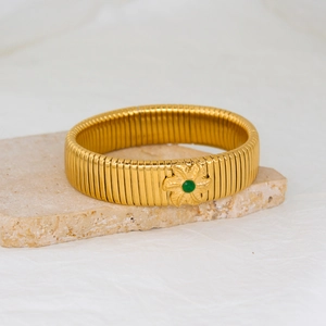 Close-up of golden flower zircon bracelet with emerald center on natural stone
