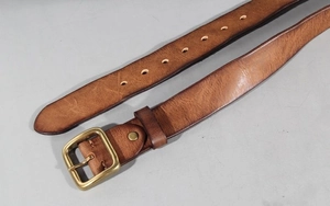 Close-up of vintage brown leather belt with aged brass buckle and textured grain