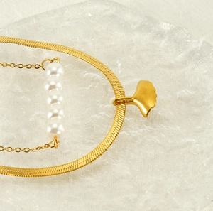 Detail of golden ginkgo leaf pendant with white pearls on a double-layer snake chain