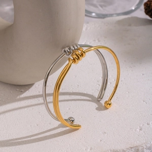 Minimalist gold and silver twisted open bangles with coiled details on a stone surface