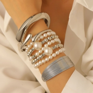 Detail of layered silver metal bracelets and white faux pearl beads on a wrist