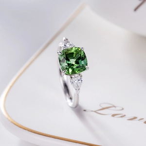 Close-up of green cushion-cut gemstone ring with silver band and white side stones
