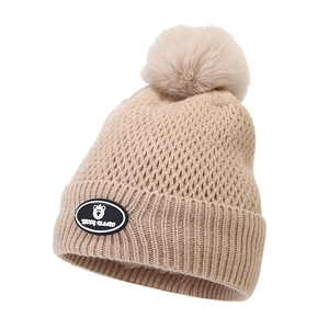 Close-up of beige knitted winter hat with faux fur pompom and teddy bear patch