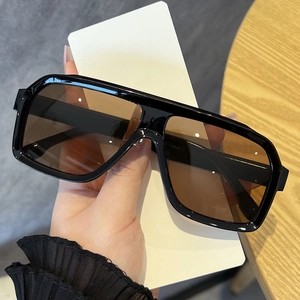 Close-up of stylish black frame sunglasses with amber lenses held by hand on wood desk