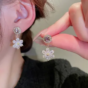 Elegant gold flower drop earrings with white zircon crystals worn by a female model