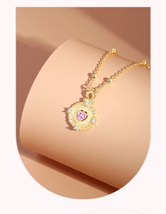 Detailaufnahme des goldenen Herzanhängers mit rosa Zirkon und strahlender Metallstruktur