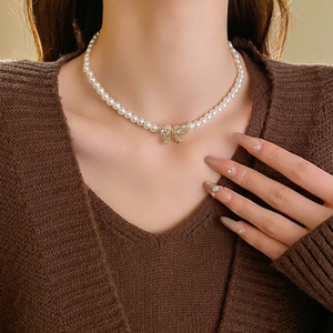Détail du collier de perles avec pendentif nœud doré serti de diamants sur mannequin