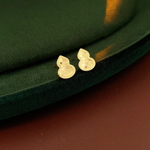 Macro detail of 18k gold plated gourd earrings on dark velvet display stand