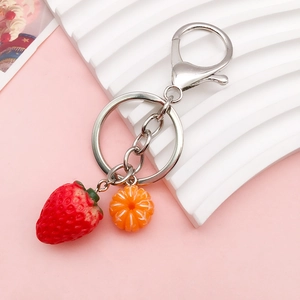 Cute acrylic strawberry and orange charms with silver keychains on pink background