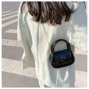 Mini black patent leather crossbody bag with gold chain shown in a lifestyle street setting