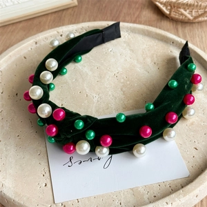 Détail d'un serre-tête en velours vert foncé avec perles colorées sur un plateau en céramique