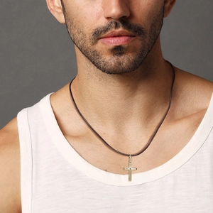 Close-up of a polished gold cross pendant on a dark brown cord worn by a male model