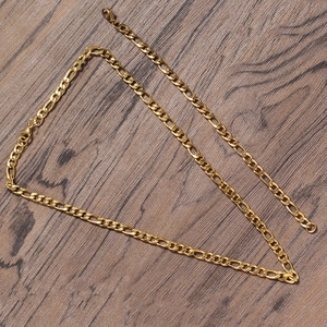 Macro shot of 5mm golden Figaro chain necklace with lobster clasp on wood texture