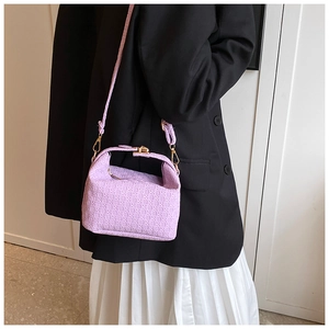 Purple woven pillow bag with gold hardware worn by a model in a stylish suit