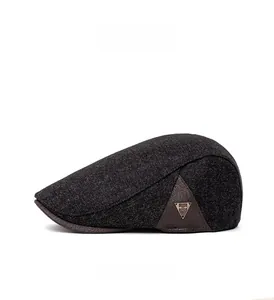 Detail view of dark grey flat cap featuring brown leather trim and metal triangle logo