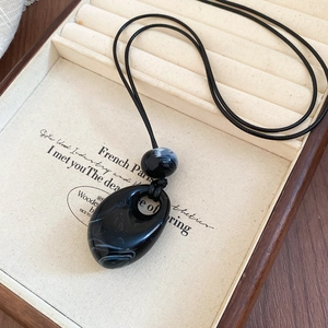 Detail of drop-shaped acrylic pendant with marble pattern and woven cord on wood tray