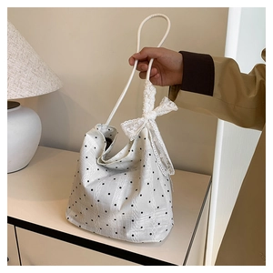 Detail view of a white bucket bag with black polka dots and a decorative lace bow handle
