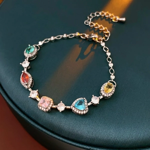 Detailed shot of multi-color gemstones on silver chain bracelet over dark teal background