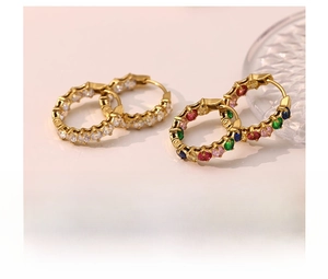 Close-up of titanium steel hoop earrings featuring colorful inlaid crystals and gold finish