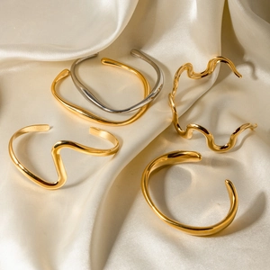 Minimalist 18k gold and silver wavy stainless steel bangles on beige silk fabric