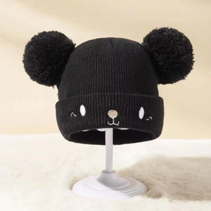 Detail einer schwarzen Baby-Strickmütze mit zwei Fellbommeln und süßer Katzenstickerei