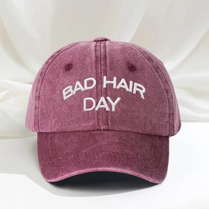 Close-up of white BAD HAIR DAY embroidery on a washed burgundy cotton baseball cap
