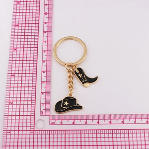 Detail view of gold cowboy hat and boot keychain with scale measurement on white background