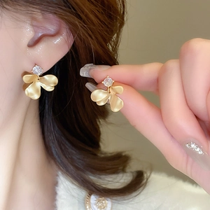 Close-up of matte gold flower earrings with round zircon stones on a model's ear