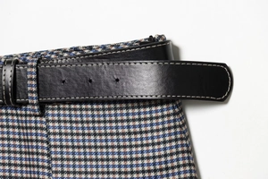 Detailed macro shot of a brown plaid skirt featuring a black leather belt with white stitching